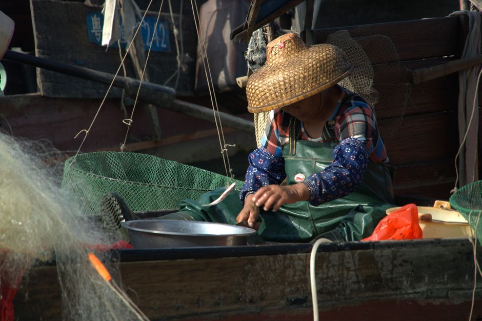 A fisherman in a straw hat and plaid shirt working on a boat with fishing nets.